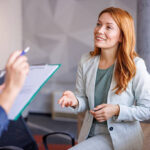 Confident professional woman discussing mastering behavioral interview questions with an interviewer holding a clipboard in a modern office setting
